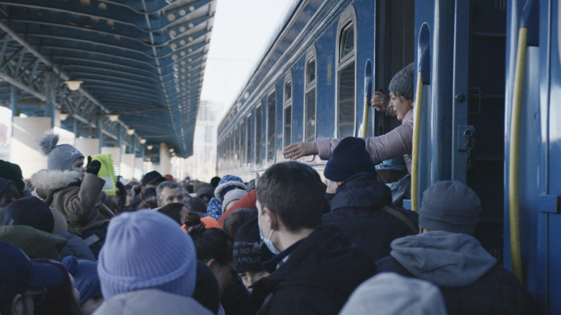 On a crowded railway platform in Kyiv's main railway station in the early days after Russia's February 2022 invasion, people help pass a small child onto the train
