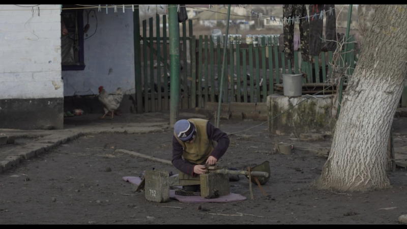 A Ukrainian boy in a village recaptured from the Russians plays at war, loading his home-made wooden machine gun