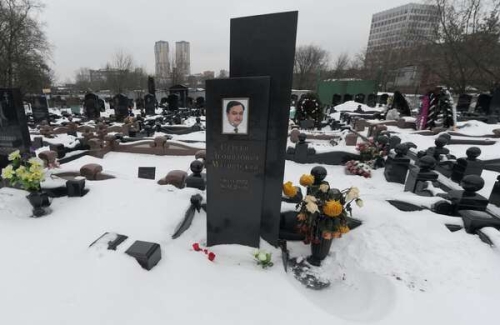 Snow-covered cemetery with a variety of tombstones and flowers, including one featuring a portrait.