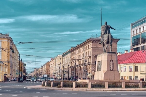 Statue of a horse-mounted figure on a city street with historic buildings and blue sky.