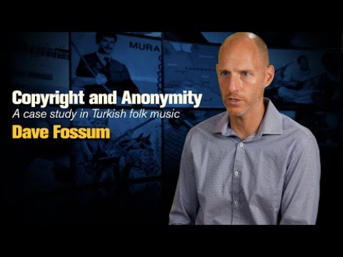 Man in a collared shirt speaking against a dark, blurred background with the text about Turkish folk music.