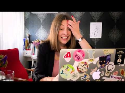 A woman smiling while looking at a sticker-covered laptop in a stylishly decorated room.