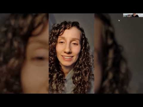 Woman with curly hair smiling, wearing a grey top, participating in an online video call.